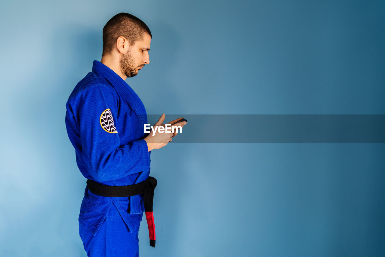 FULL LENGTH OF MAN LOOKING AWAY WHILE STANDING ON BLUE PHONE