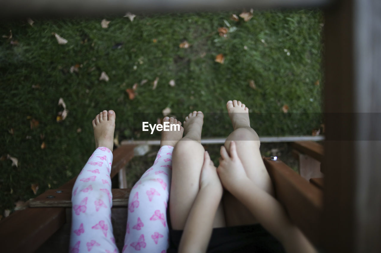 Low section of sisters sitting on outdoor play equipment at playground