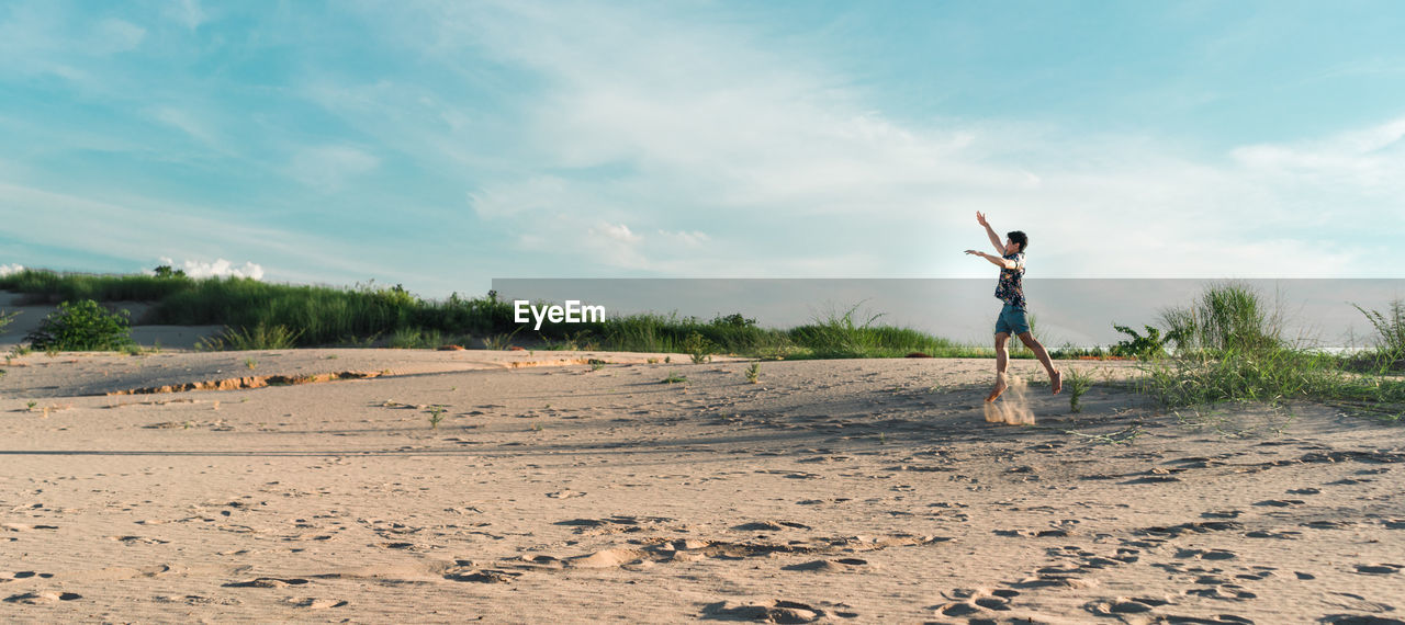 Man with arms raised on beach against sky