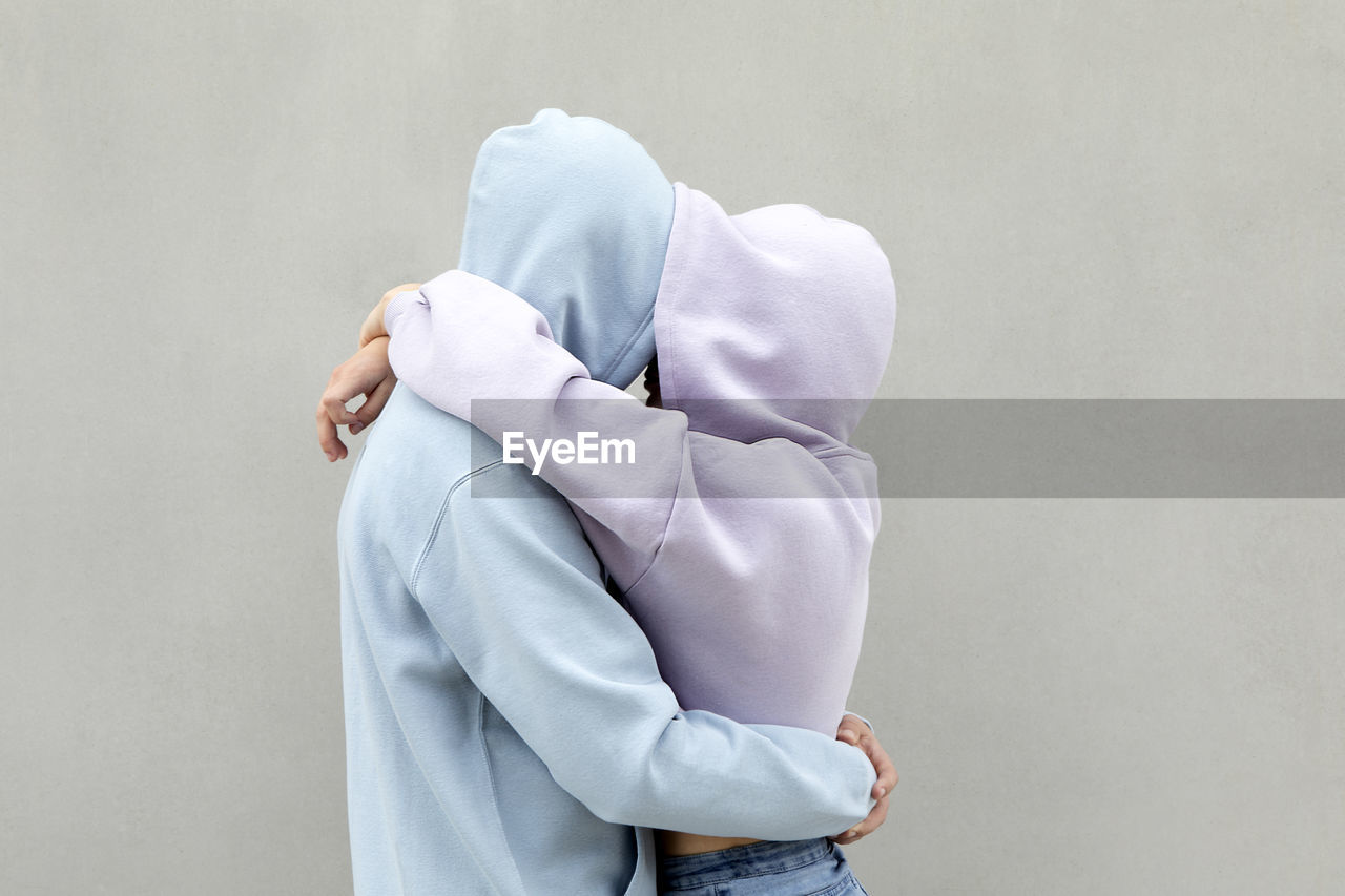 Couple in hooded shirt embracing each other by wall