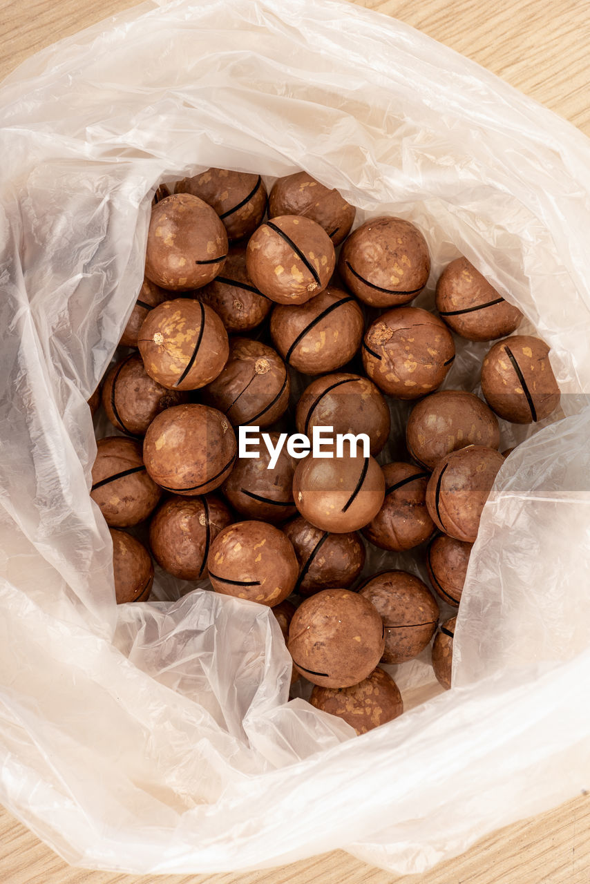 Top view of unpeeled macadamia nuts in a plastic bag on a wooden table.