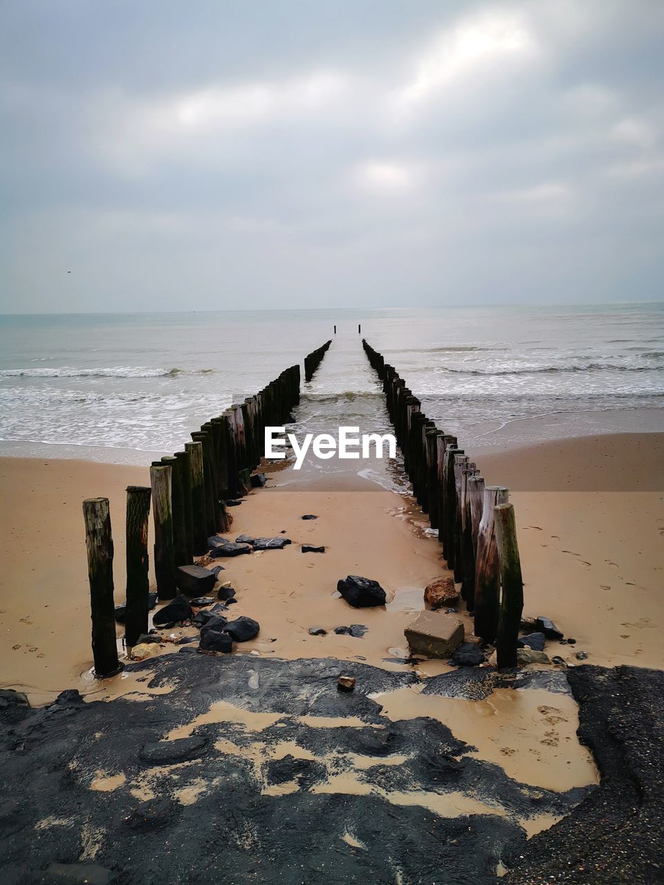 Wooden posts on beach by sea against sky