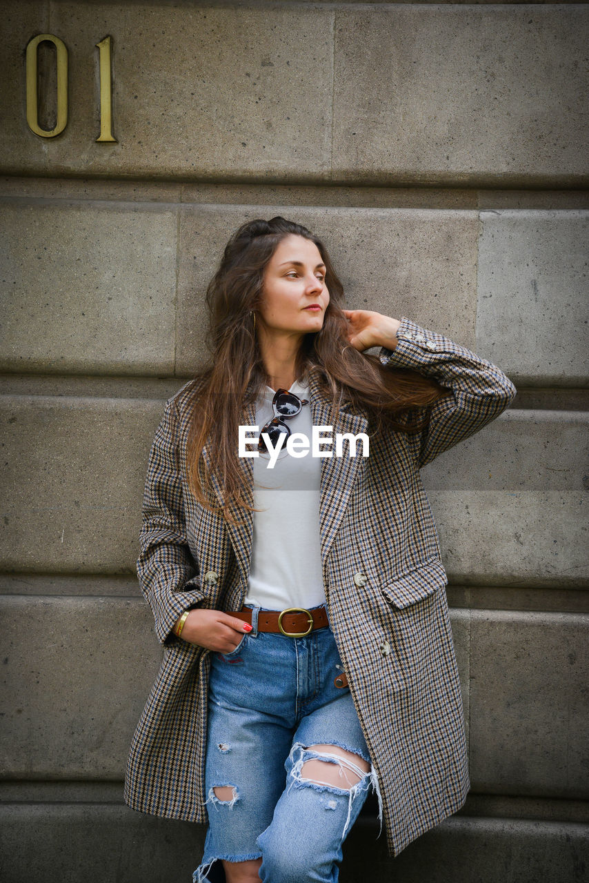 Beautiful woman looking away while standing against wall