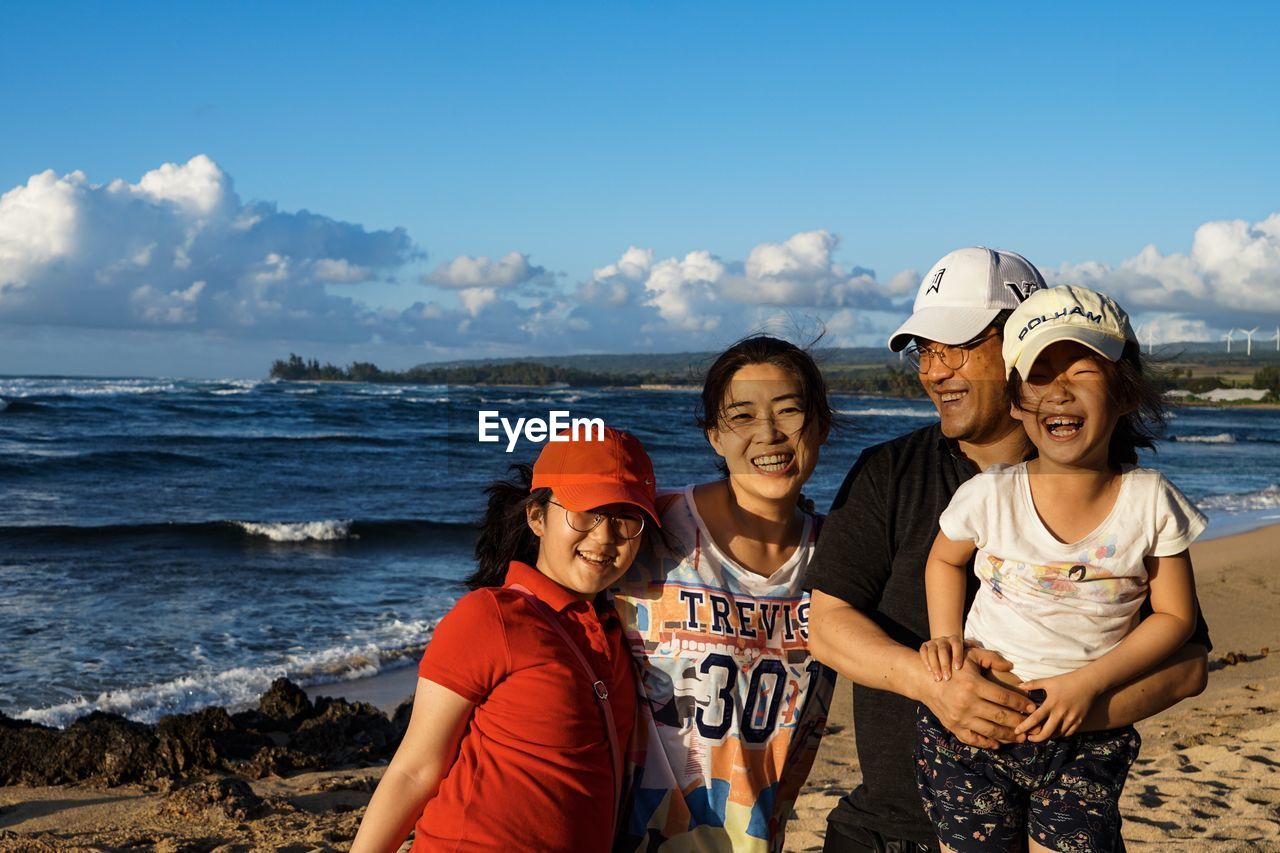 PORTRAIT OF SMILING FRIENDS ON BEACH AGAINST SEA AGAINST SKY