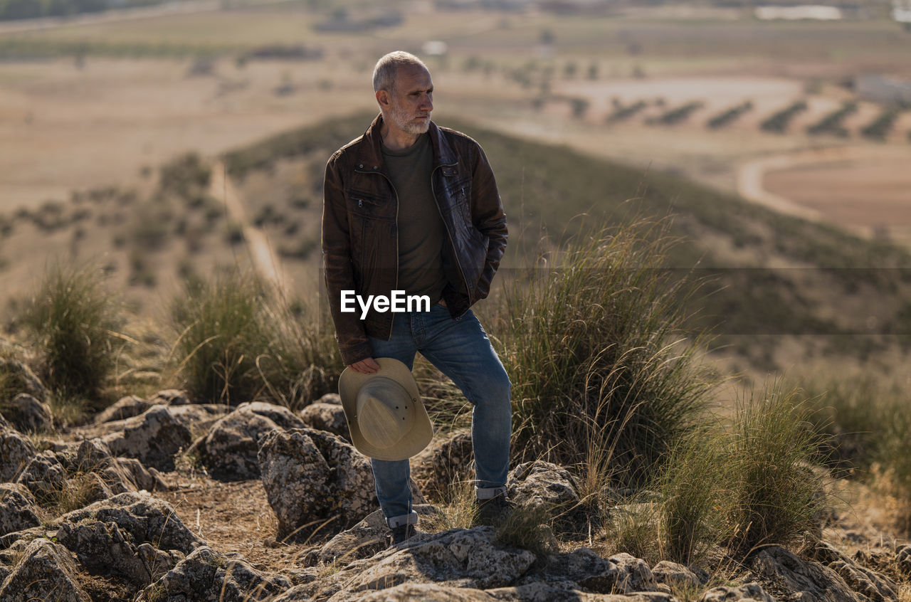 Portrait of adult man with brown leather jacket standing on top of hill