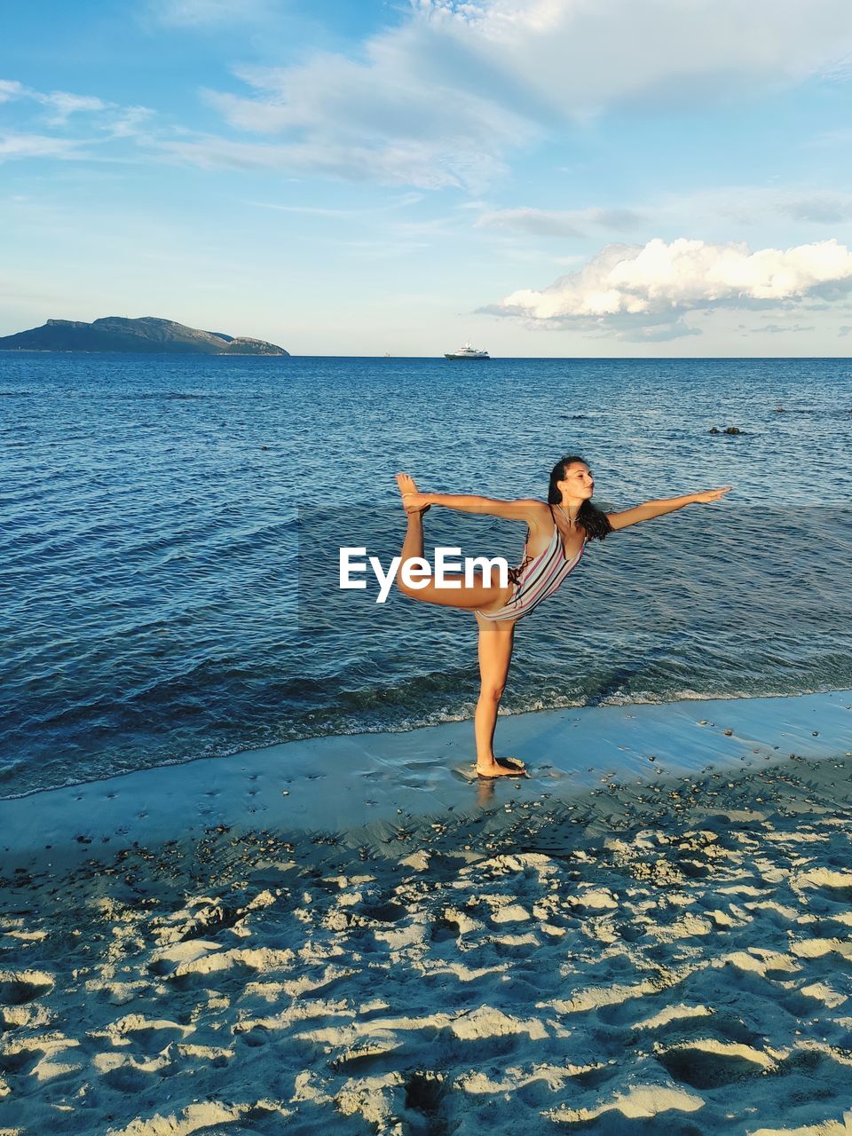 Gymnast standing on beach by sea against sky