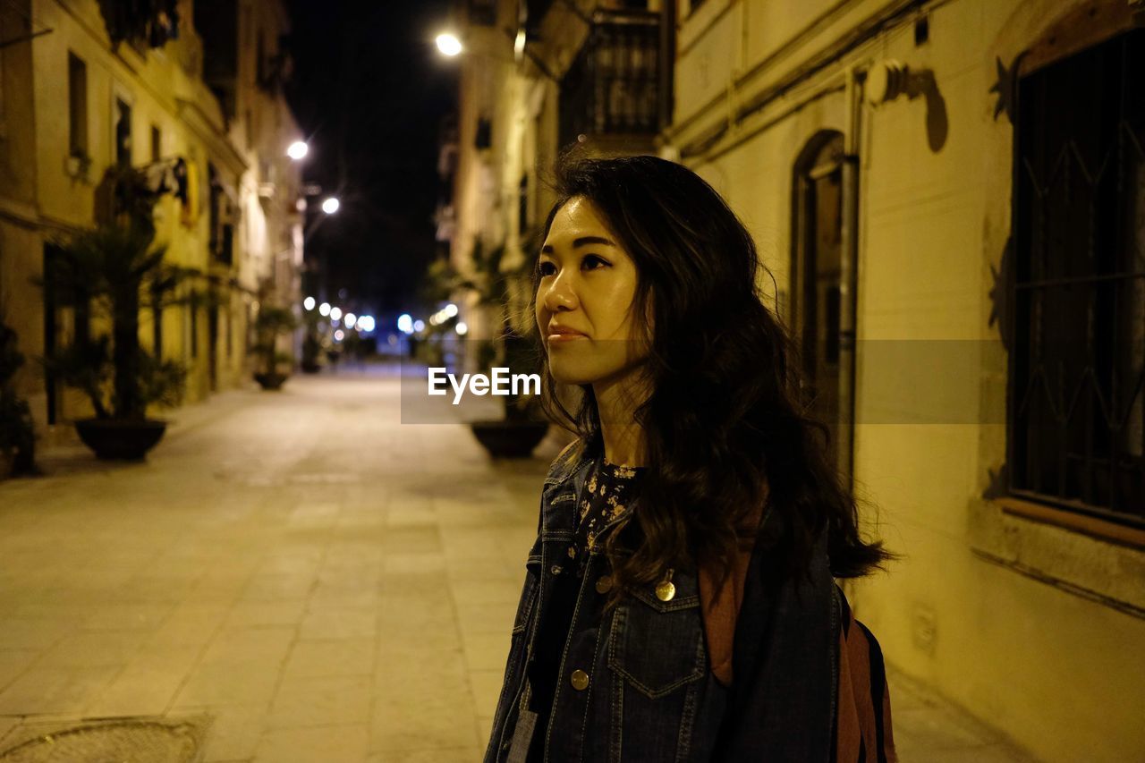 Portrait of woman standing on illuminated street at night