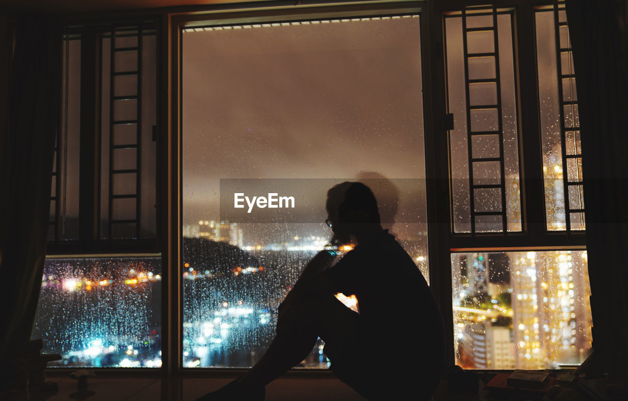 Rear view of woman looking through window at night