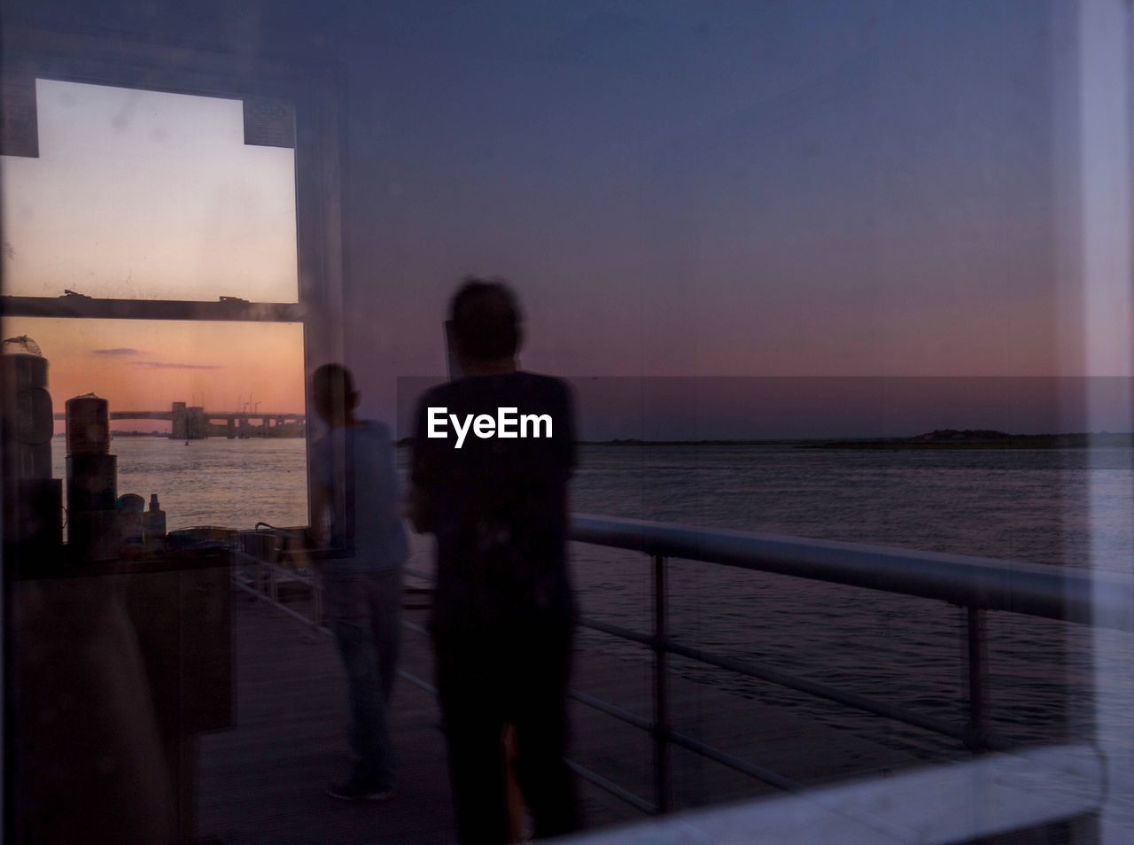 PEOPLE STANDING BY RAILING AT SEA AGAINST SKY