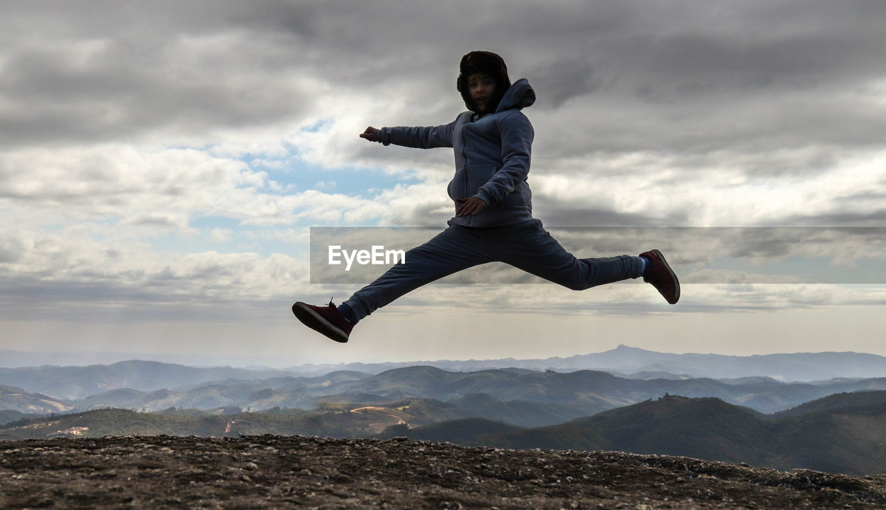 Portrait of boy jumping on land against mountains and sky