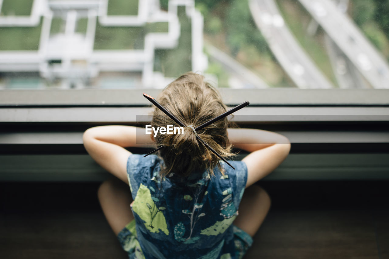 High angle view of girl with japanese hairpins looking through window while sitting at home