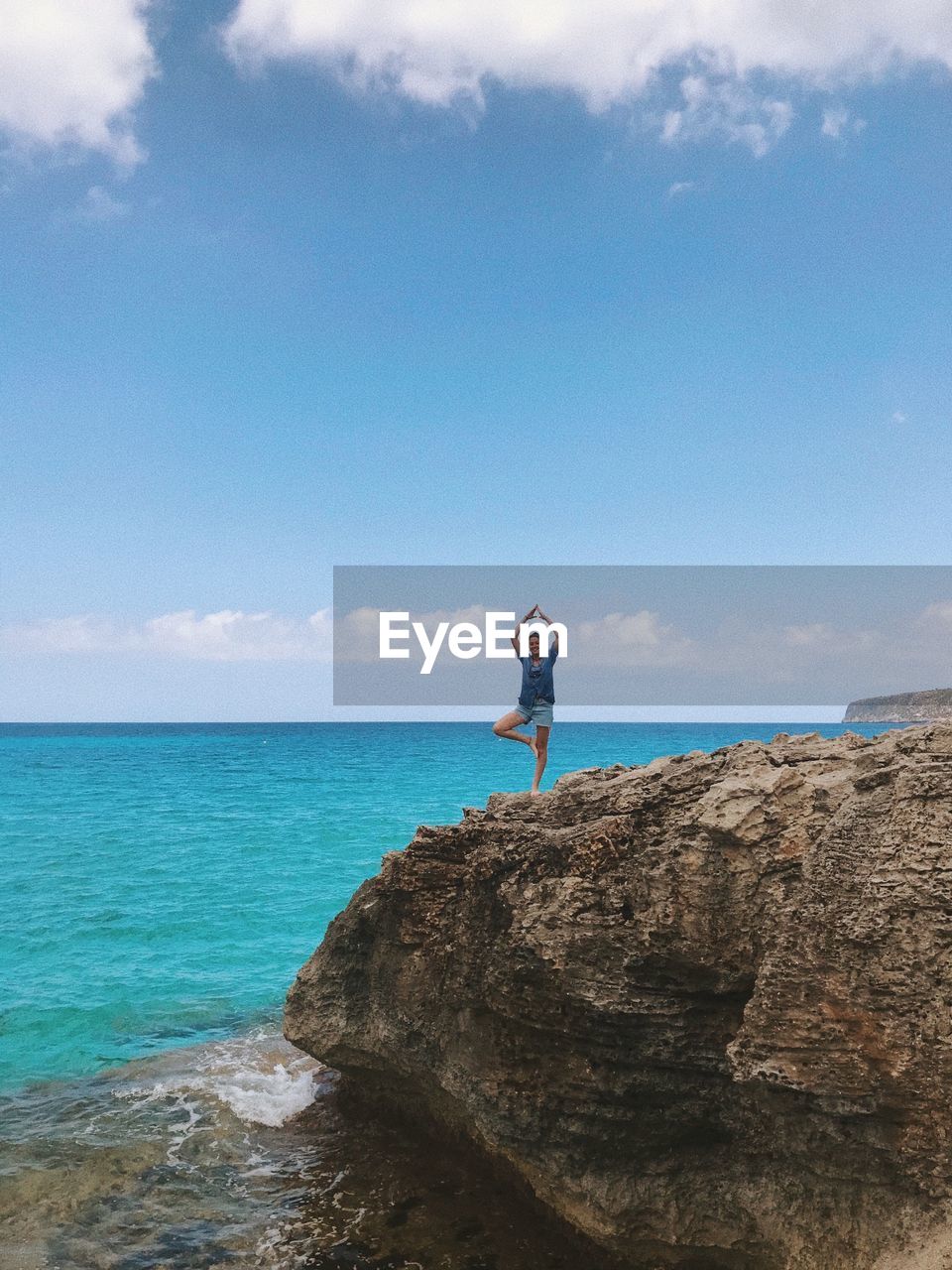 Woman standing on rocky shore against blue sky