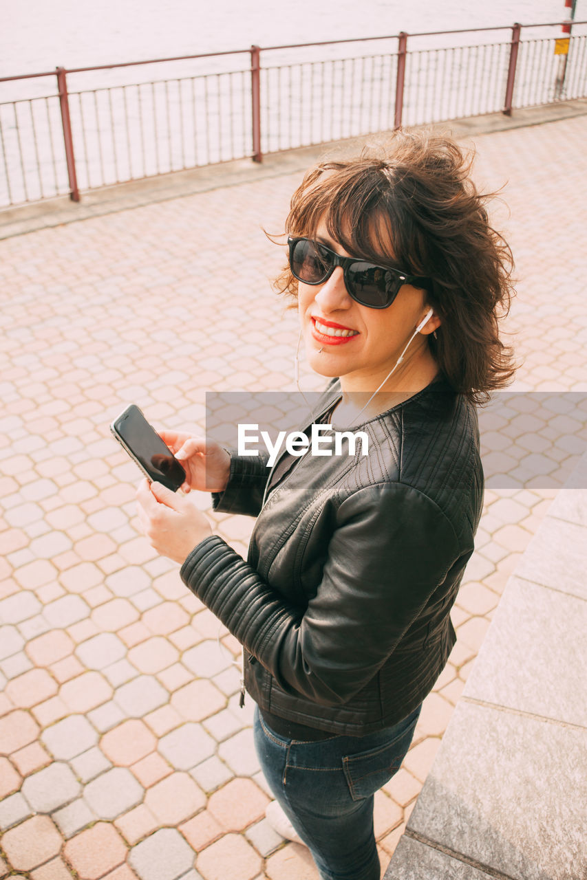 Portrait of smiling mid adult woman using mobile phone on footpath