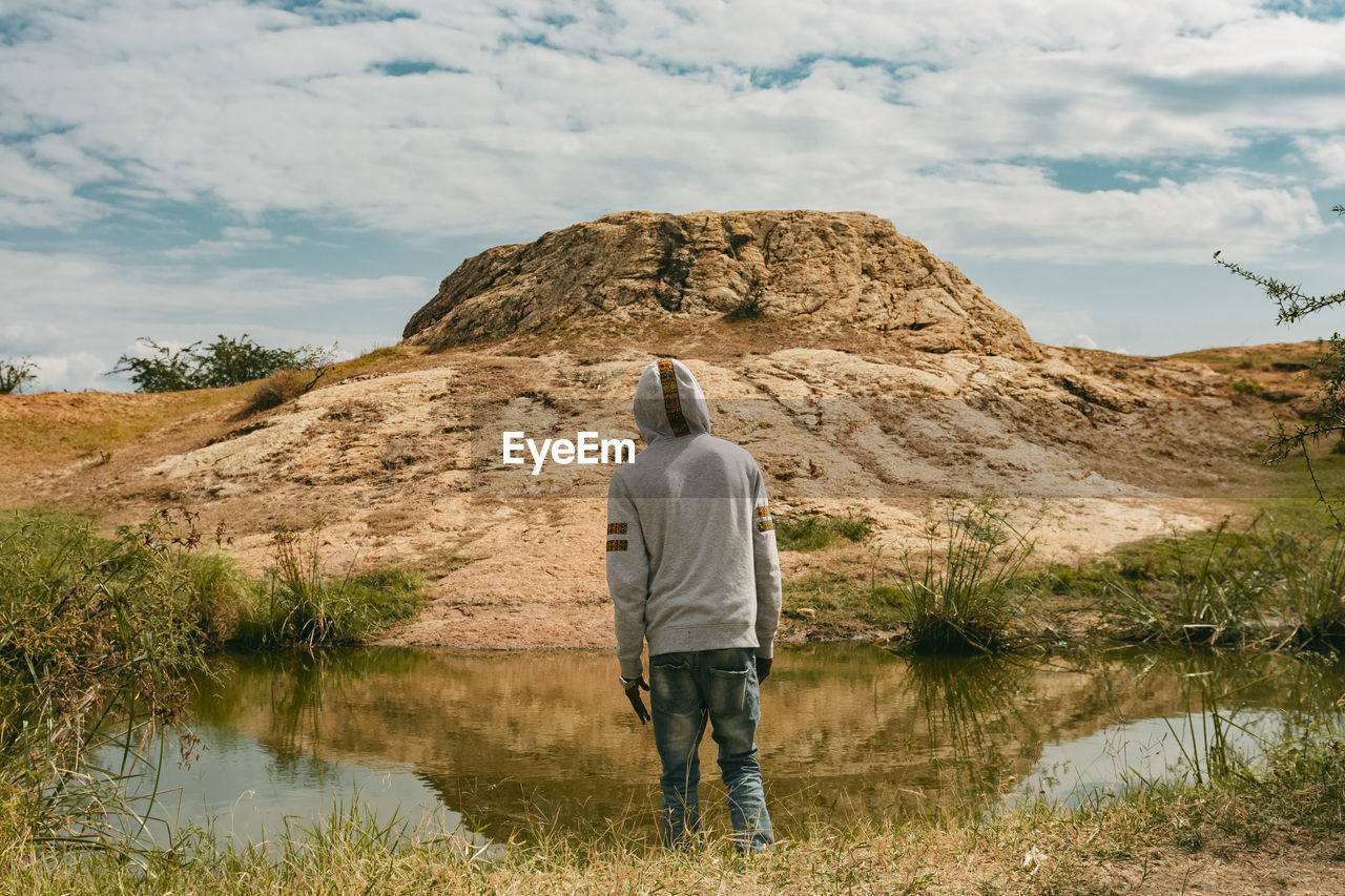 A man standing infront of water looking at a big rock object