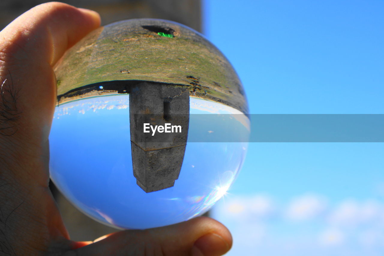 Cropped hand holding crystal ball with reflection on tower against blue sky