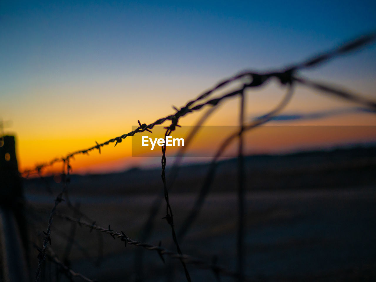 CLOSE-UP OF BARBED WIRE FENCE DURING SUNSET