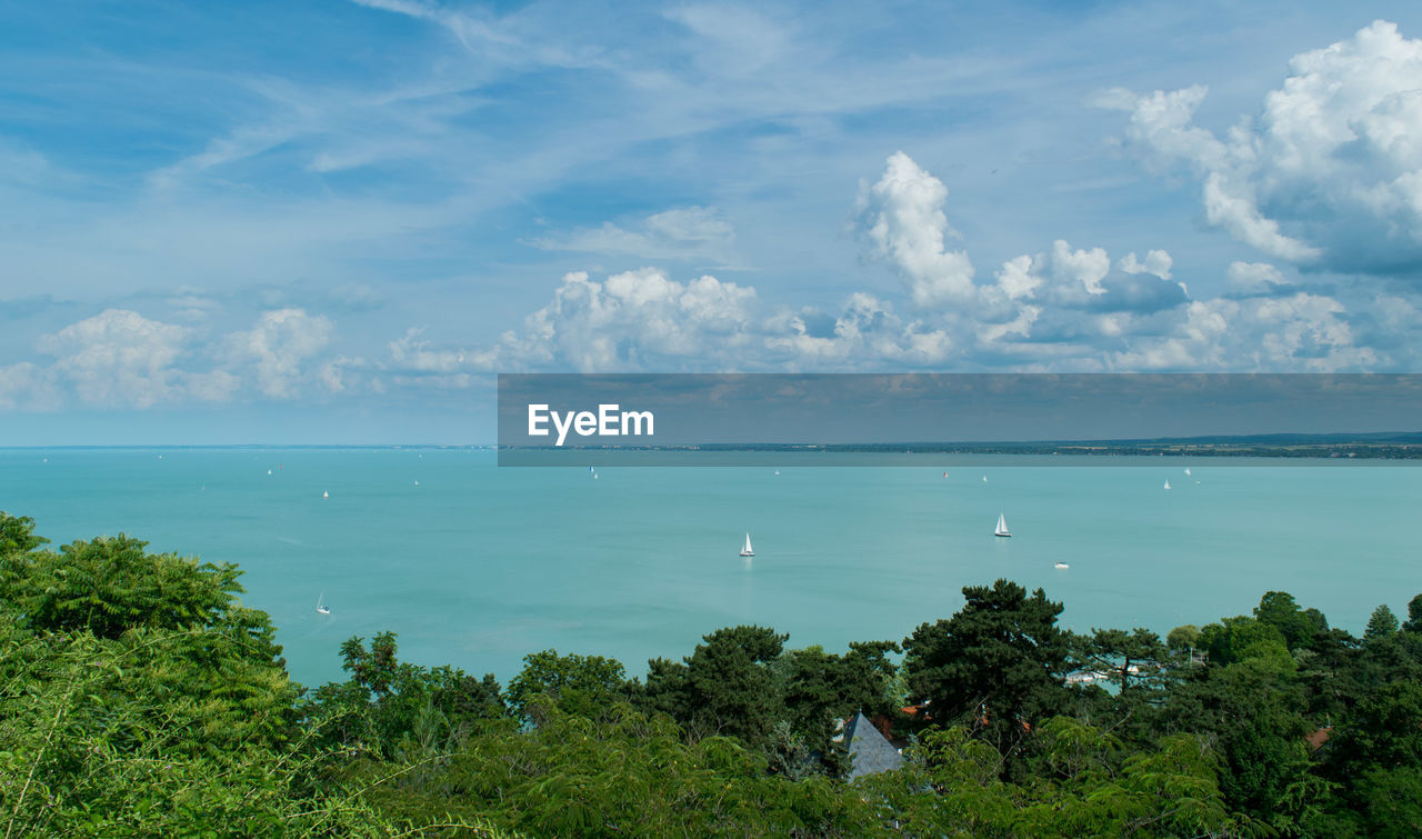 Scenic view of sea by trees against cloudy sky