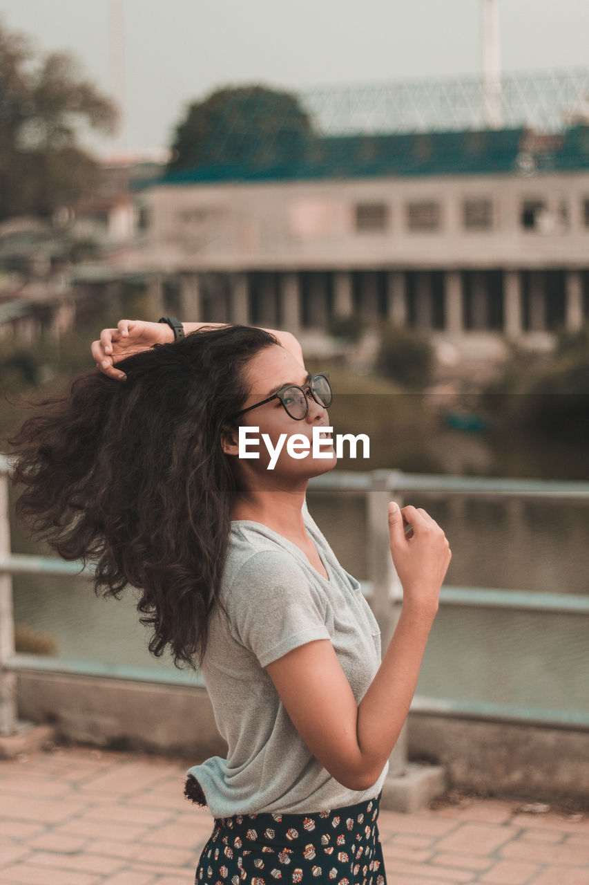 Young woman with hand in hair looking away standing against railing