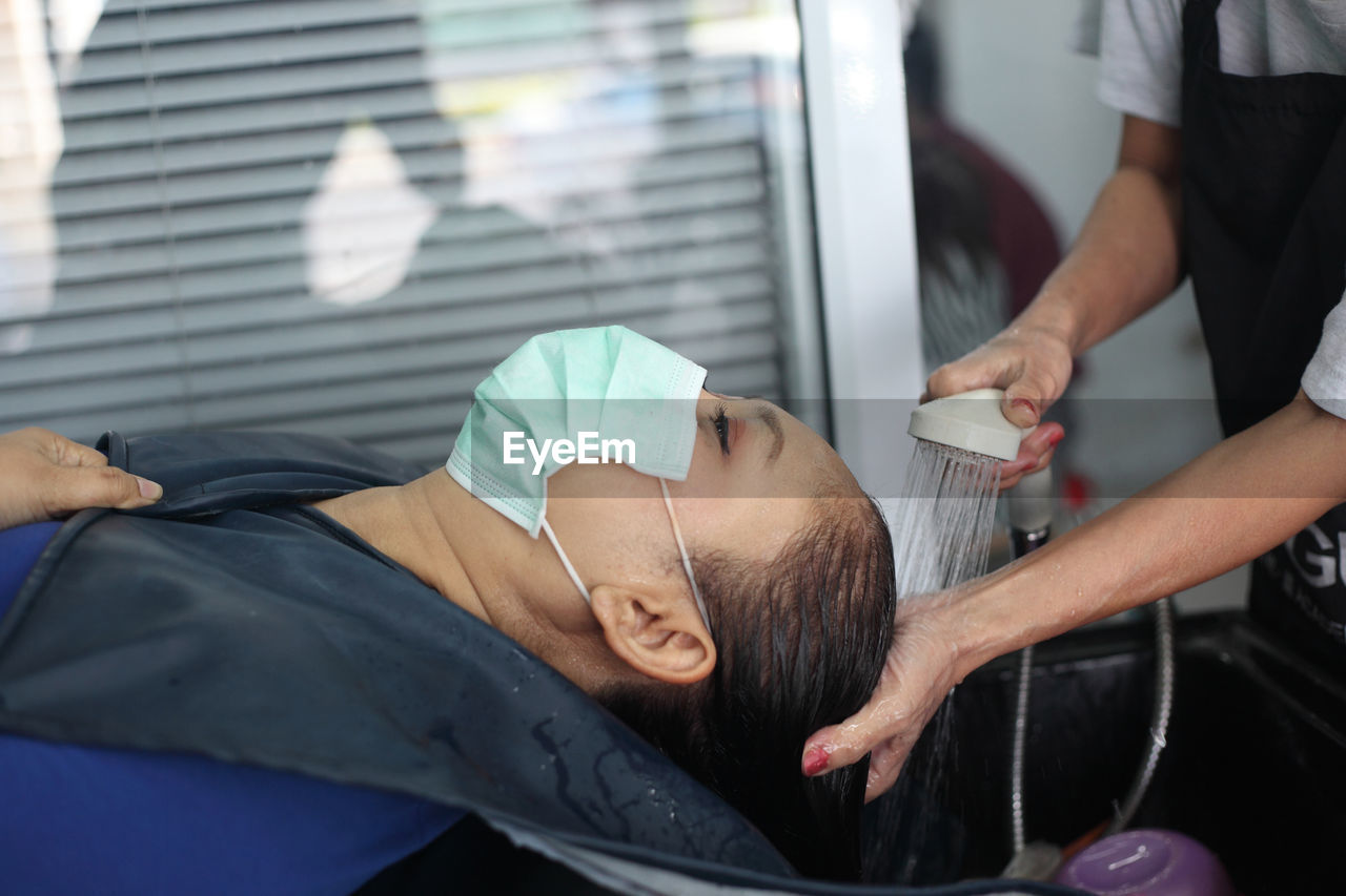 Midsection of hairdresser washing woman hair in salon