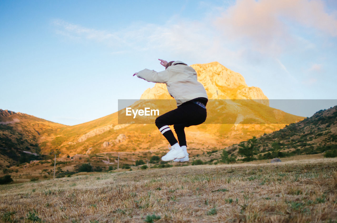 Back view of unrecognizable male in casual clothes jumping high against mountains