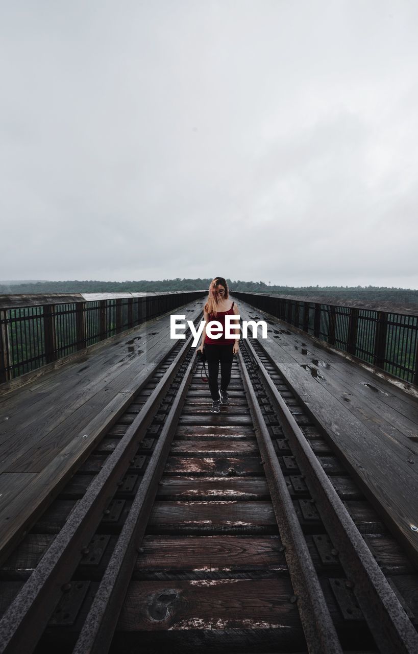 Woman walking on railroad track over rail bridge against sky