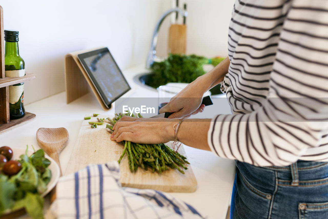 Young woman cooking at home using digital tablet for recipe