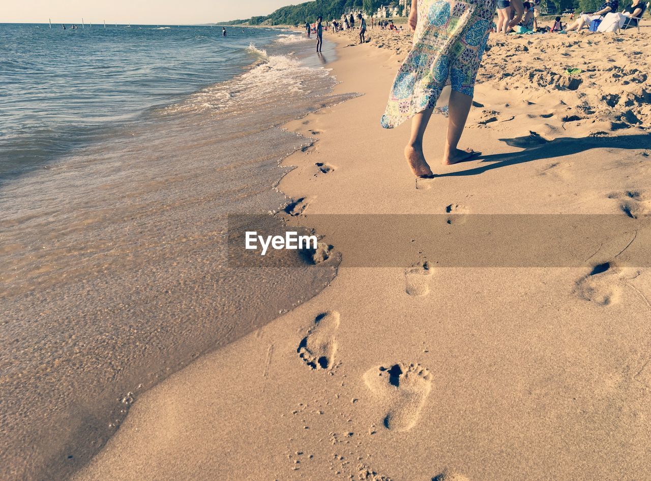 LOW SECTION OF MAN ON BEACH AGAINST SKY