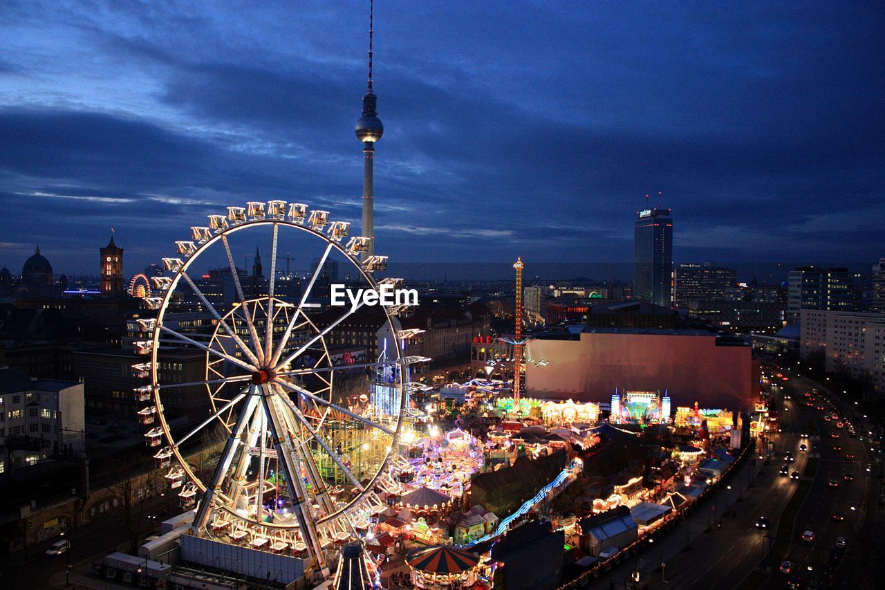 Ferris wheel and fernsehturm tower in city at christmas market against cloudy sky