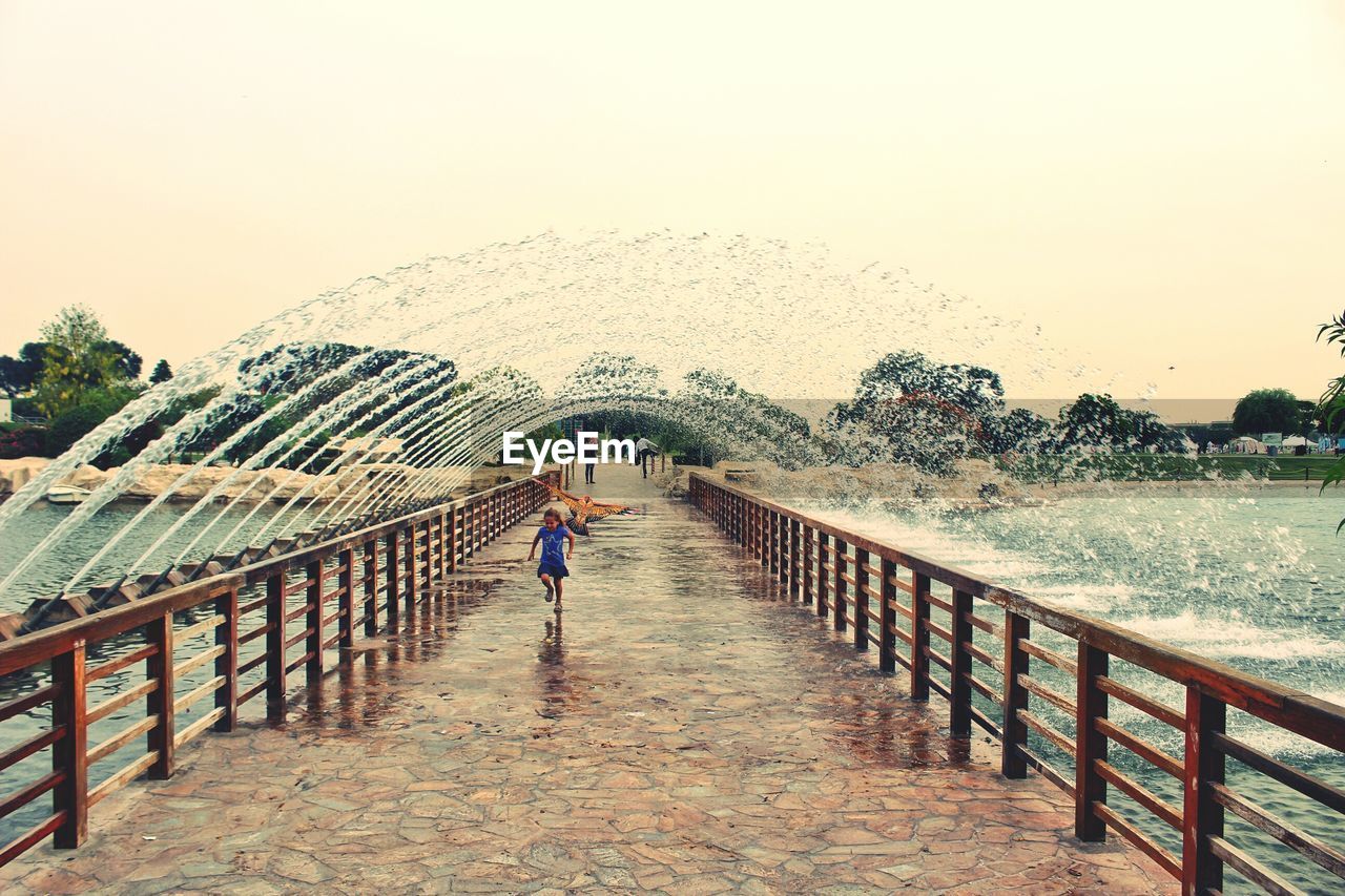 REAR VIEW OF WOMAN STANDING ON FOOTBRIDGE AGAINST SKY