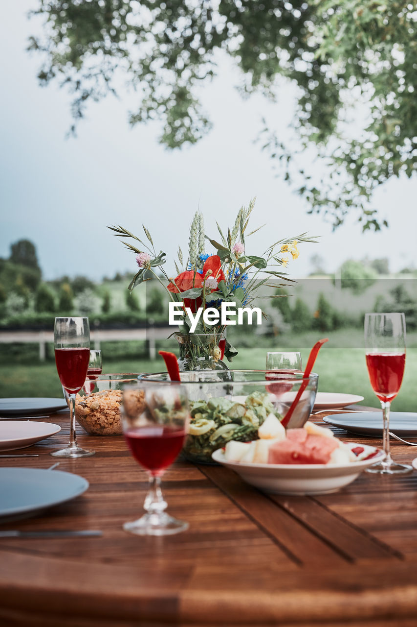 Dinner in an apple orchard garden on wooden table with salads and wine decorated with flowers