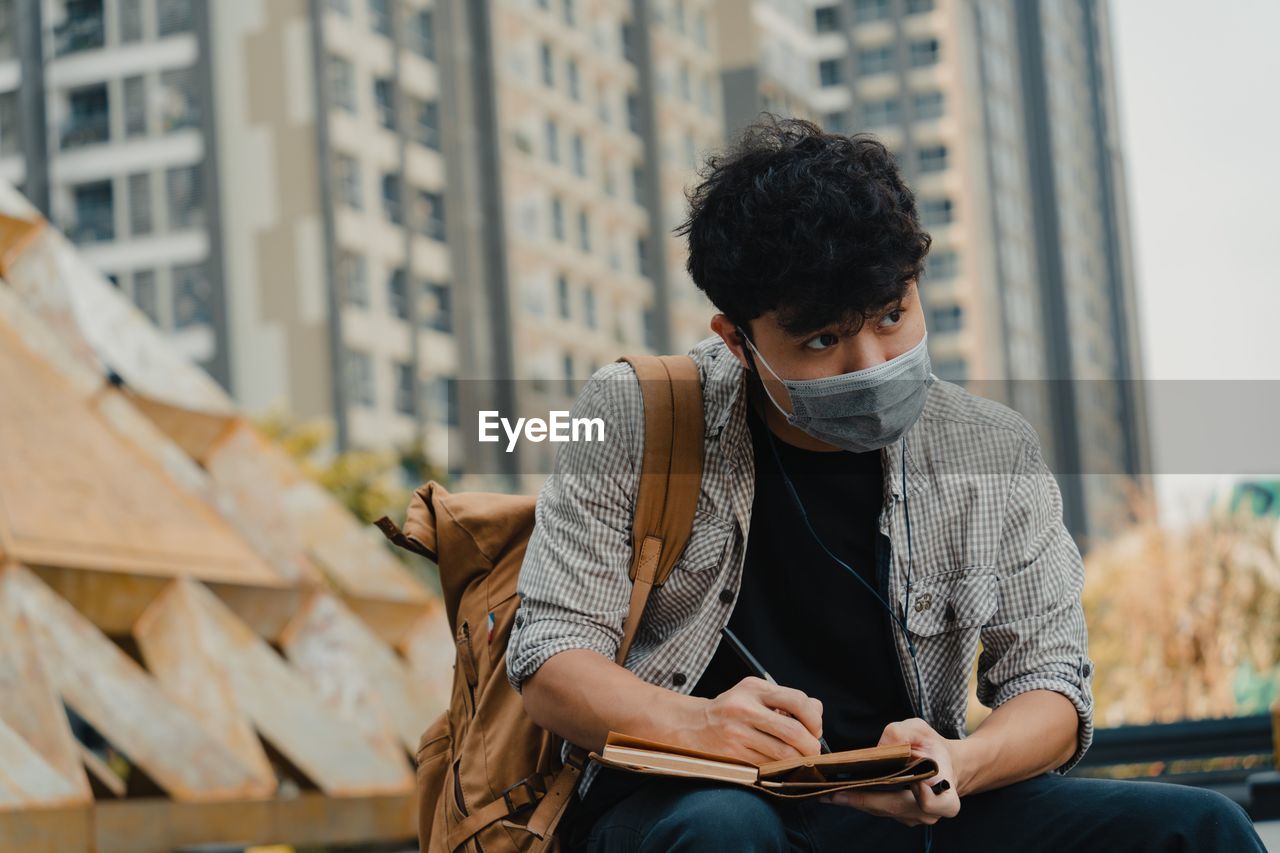 Young man wearing mask writing on diary