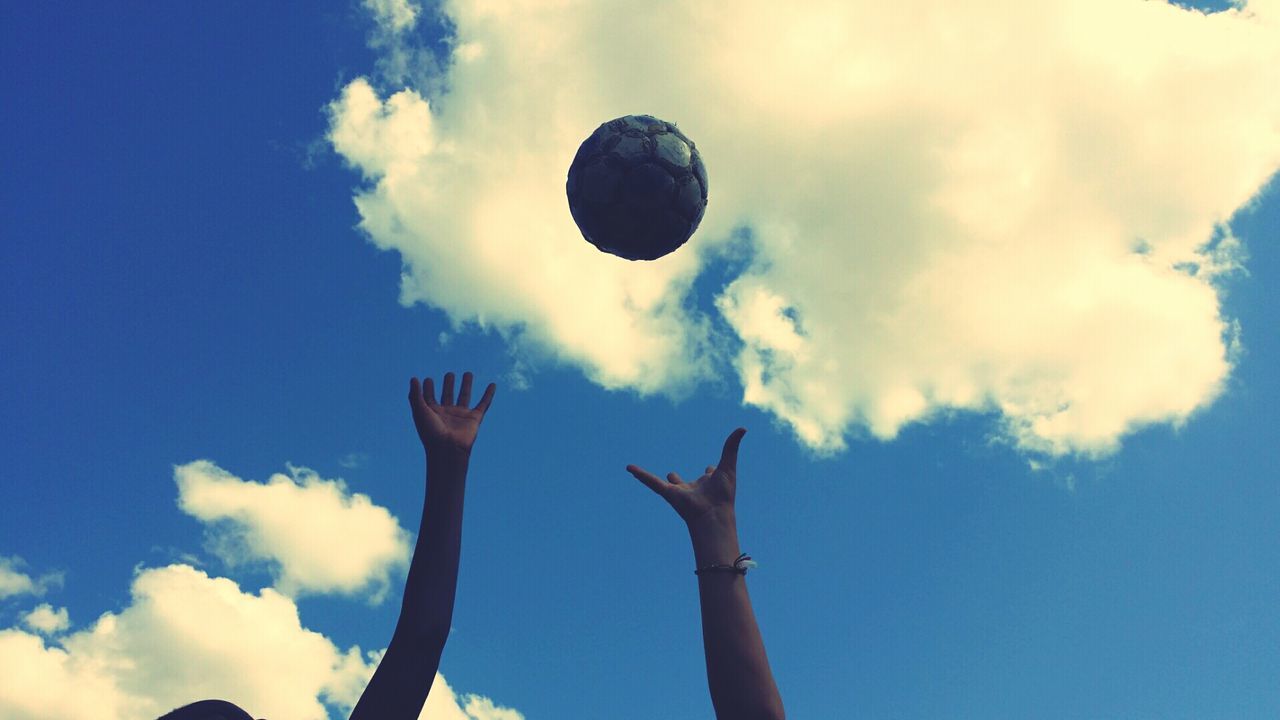 Hands reaching for soccer ball against cloudy sky