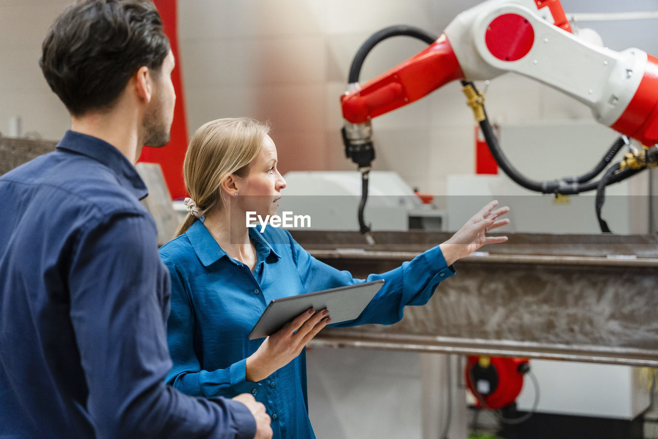 Engineer gesturing and explaining colleague in robot factory