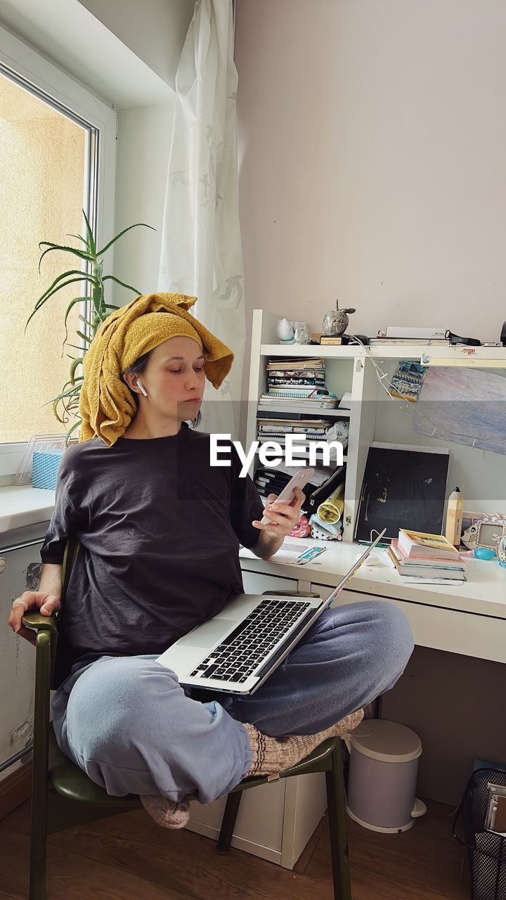 Woman wearing a yellow scarf with a laptop and mobile phone working in her home office