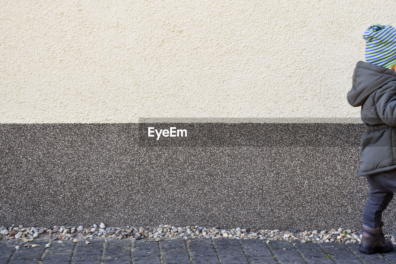 Cropped image of child walking on footpath by wall