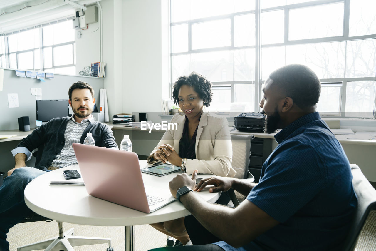 Smiling business people looking at laptop computer during discussion in office