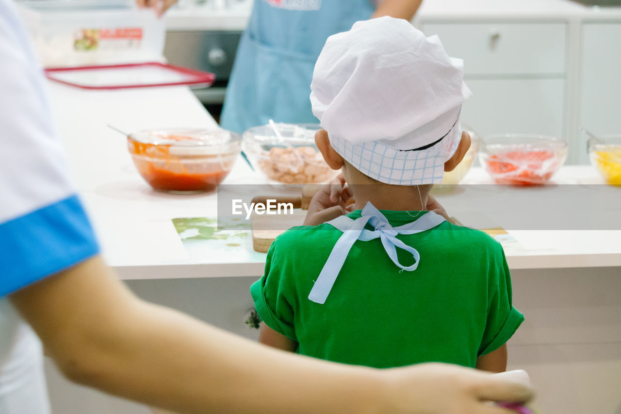 Rear view of boy in chef hat cooking food in kitchen