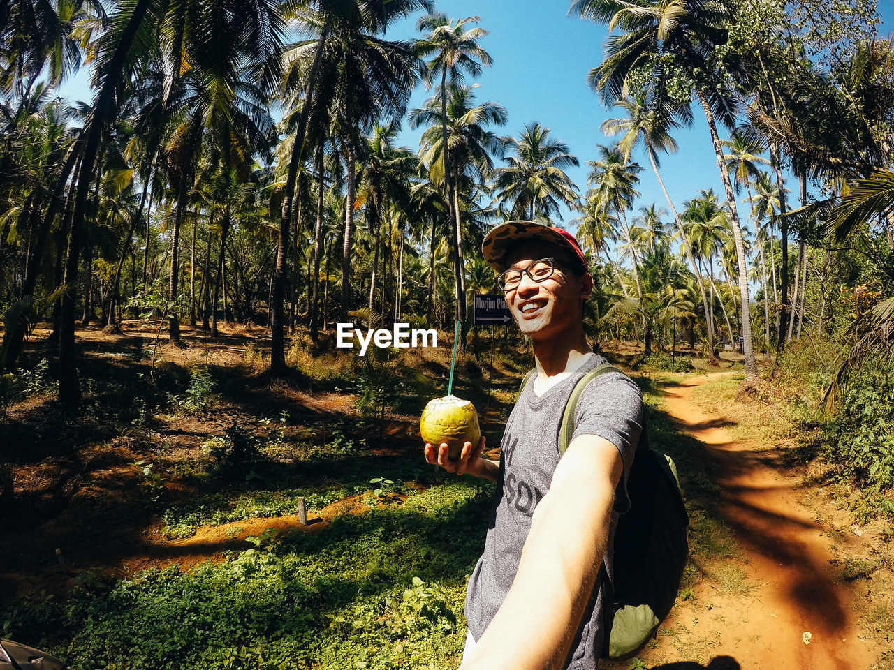 Smiling young man holding coconut water on field during sunny day