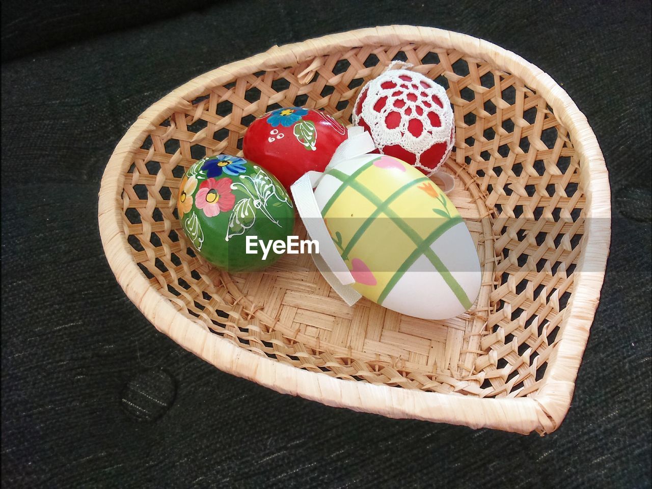 High angle view of multi colored easter eggs in heart shape wicker basket on table