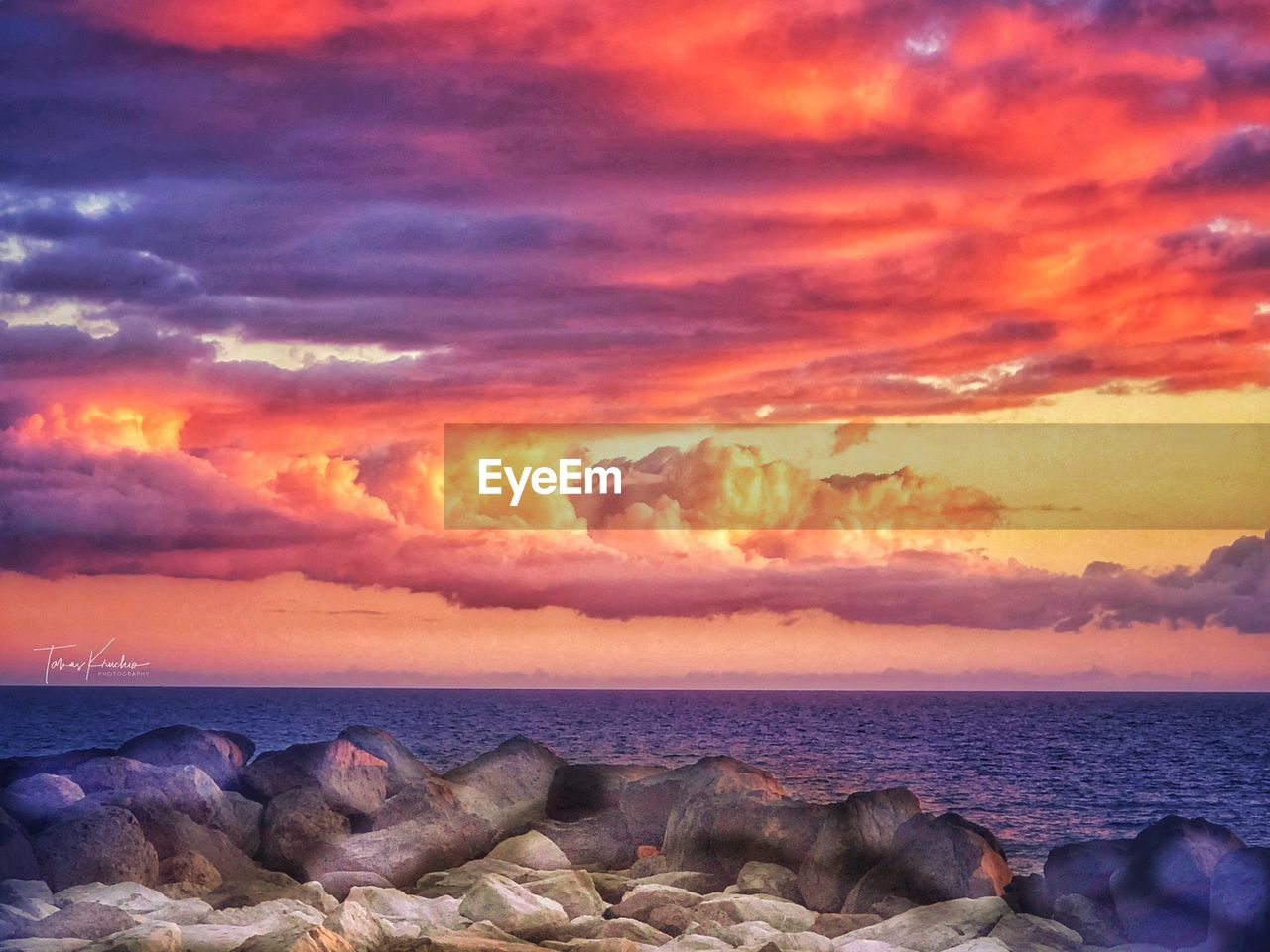 ROCKS BY SEA AGAINST ORANGE SKY