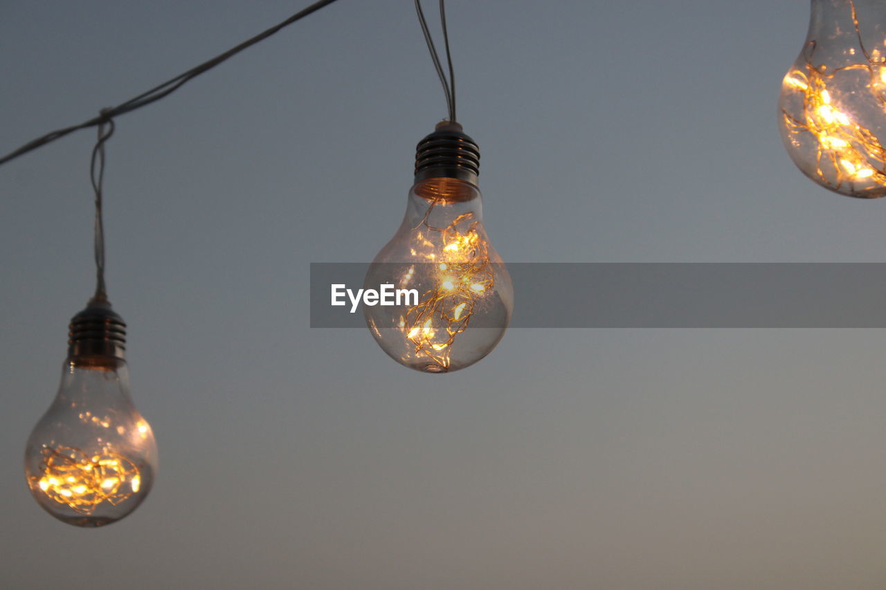 Low angle view of illuminated light bulb against sky