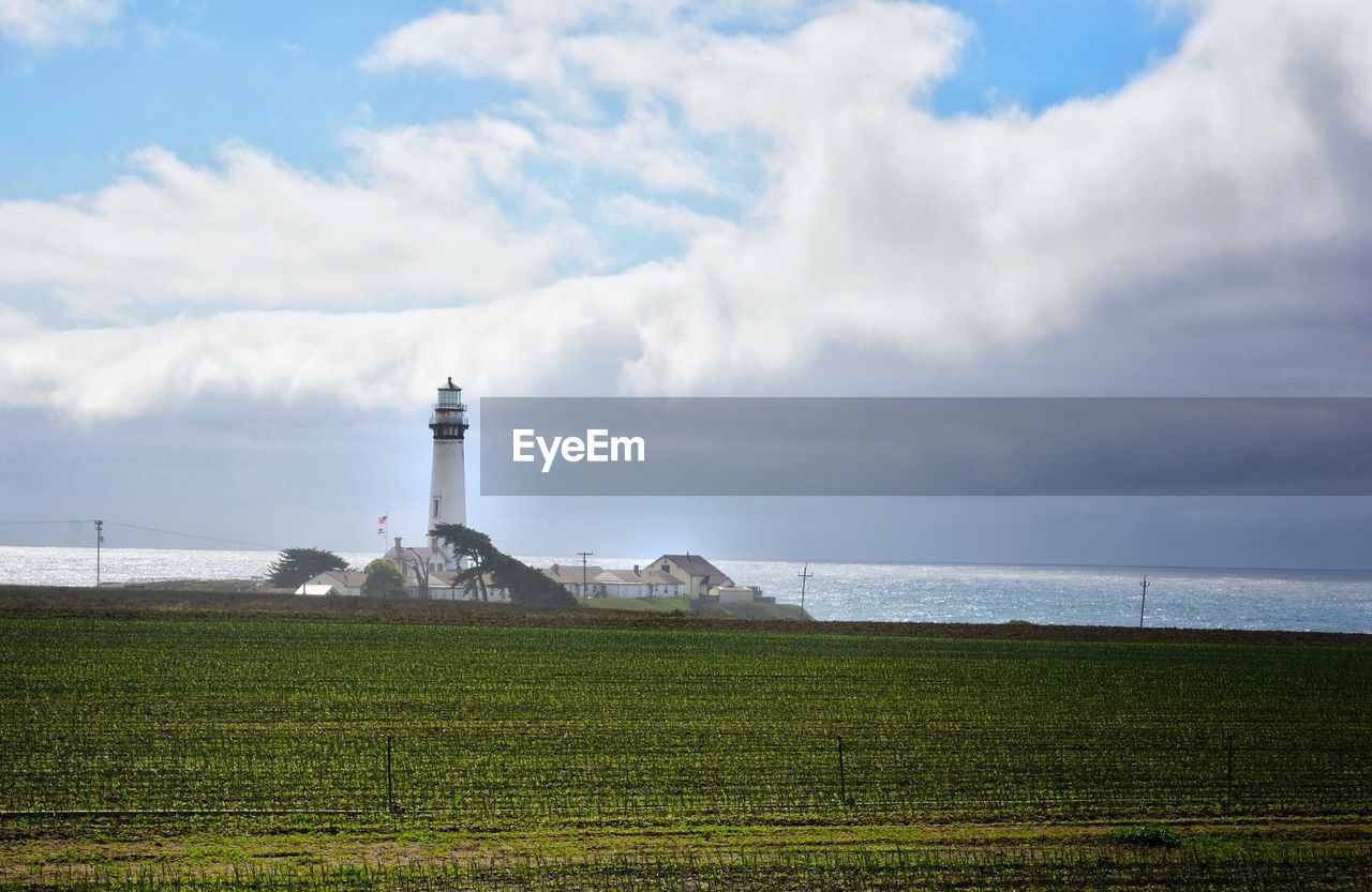 Agricultural field by pigeon point lighthouse against cloudy sky
