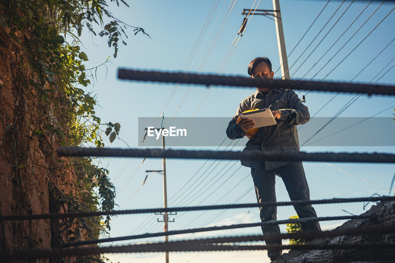 MAN ON ELECTRICITY PYLONS AGAINST SKY