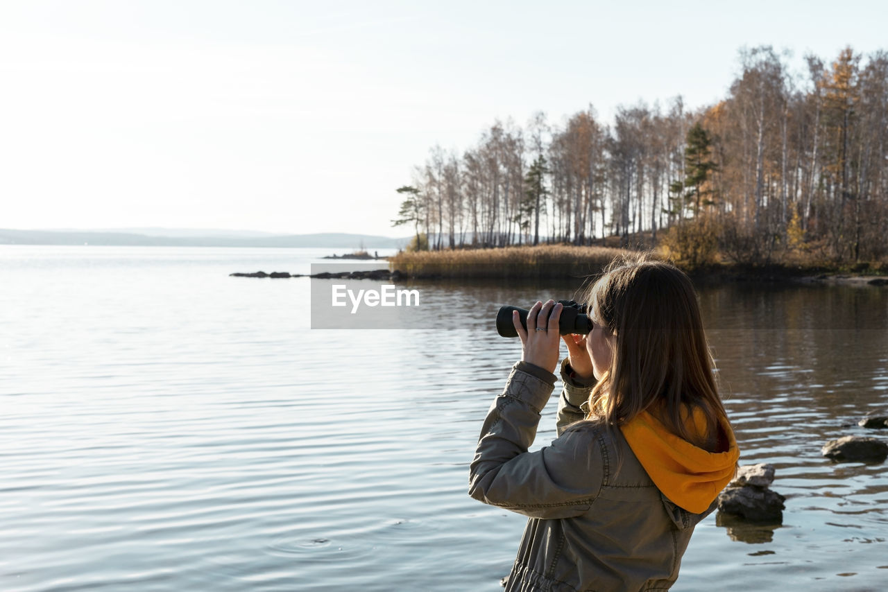 Woman looking through binoculars at birds on lake bird watching, ecology research nature, reserve