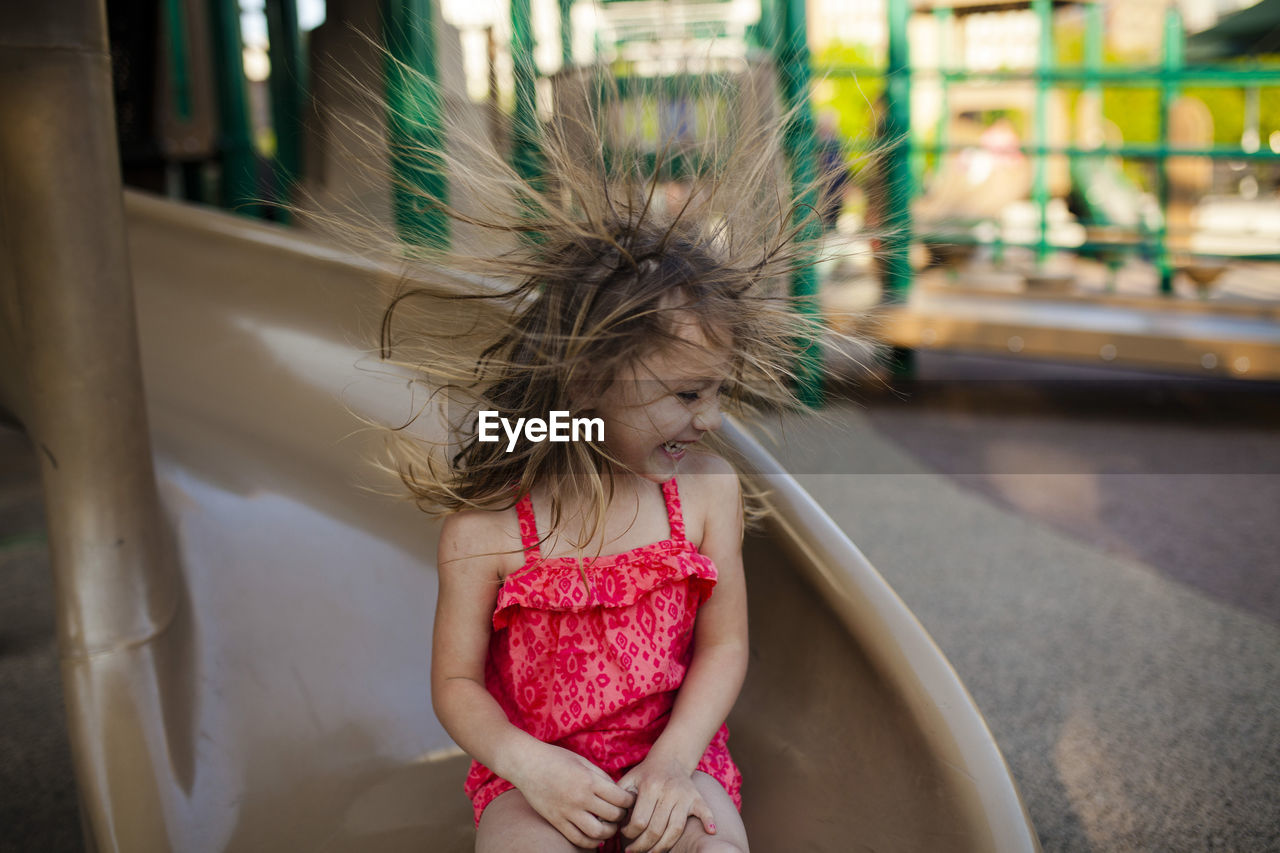 Happy girl playing flicking hair while sitting on slide