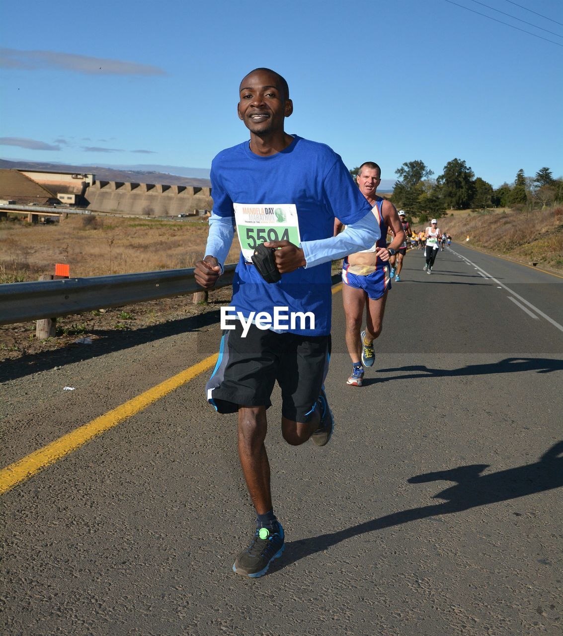 Portrait of mid adult man running on road against blue sky during sunny day