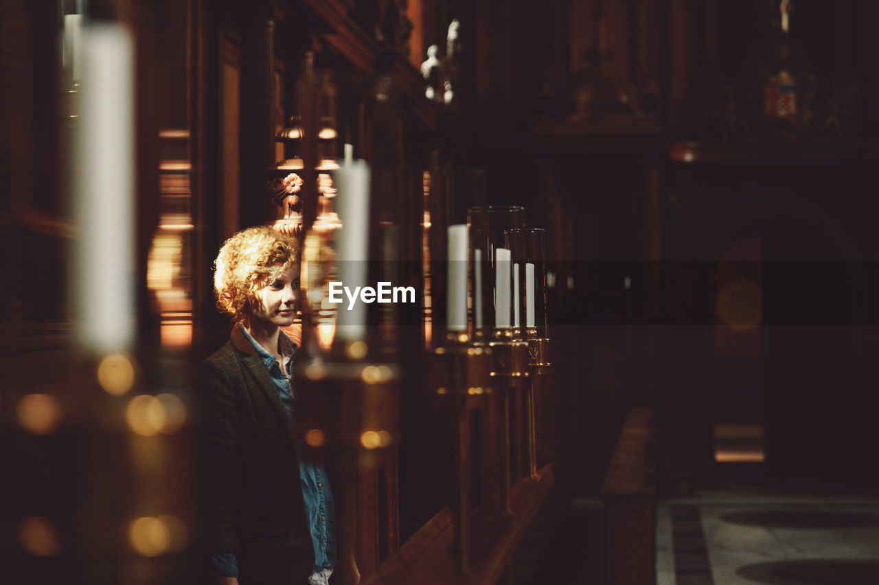Thoughtful young woman standing by candles in church