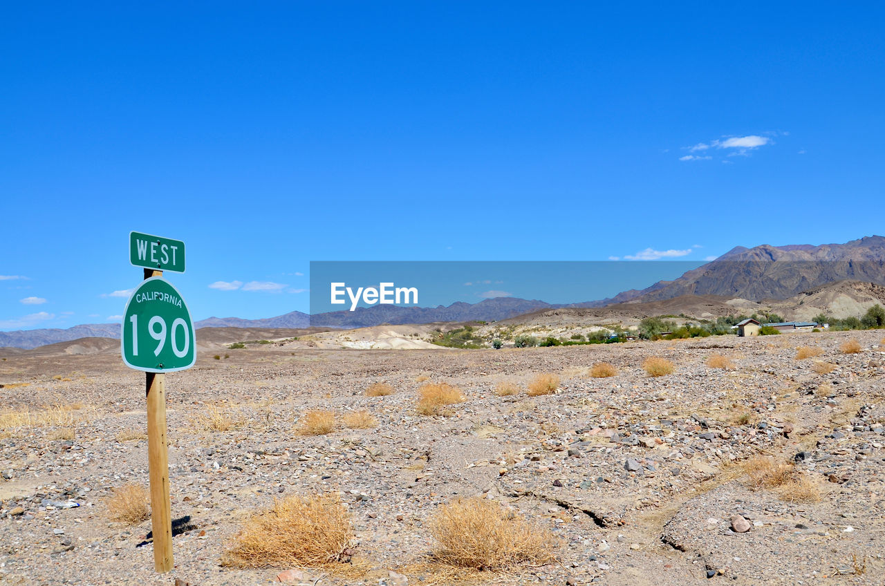 ROAD SIGN AGAINST MOUNTAIN BLUE SKY