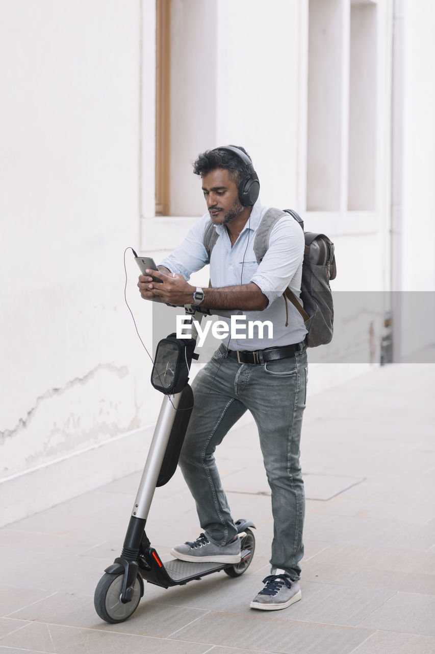 Casual businessman with headphones, smartphone and e-scooter in the city