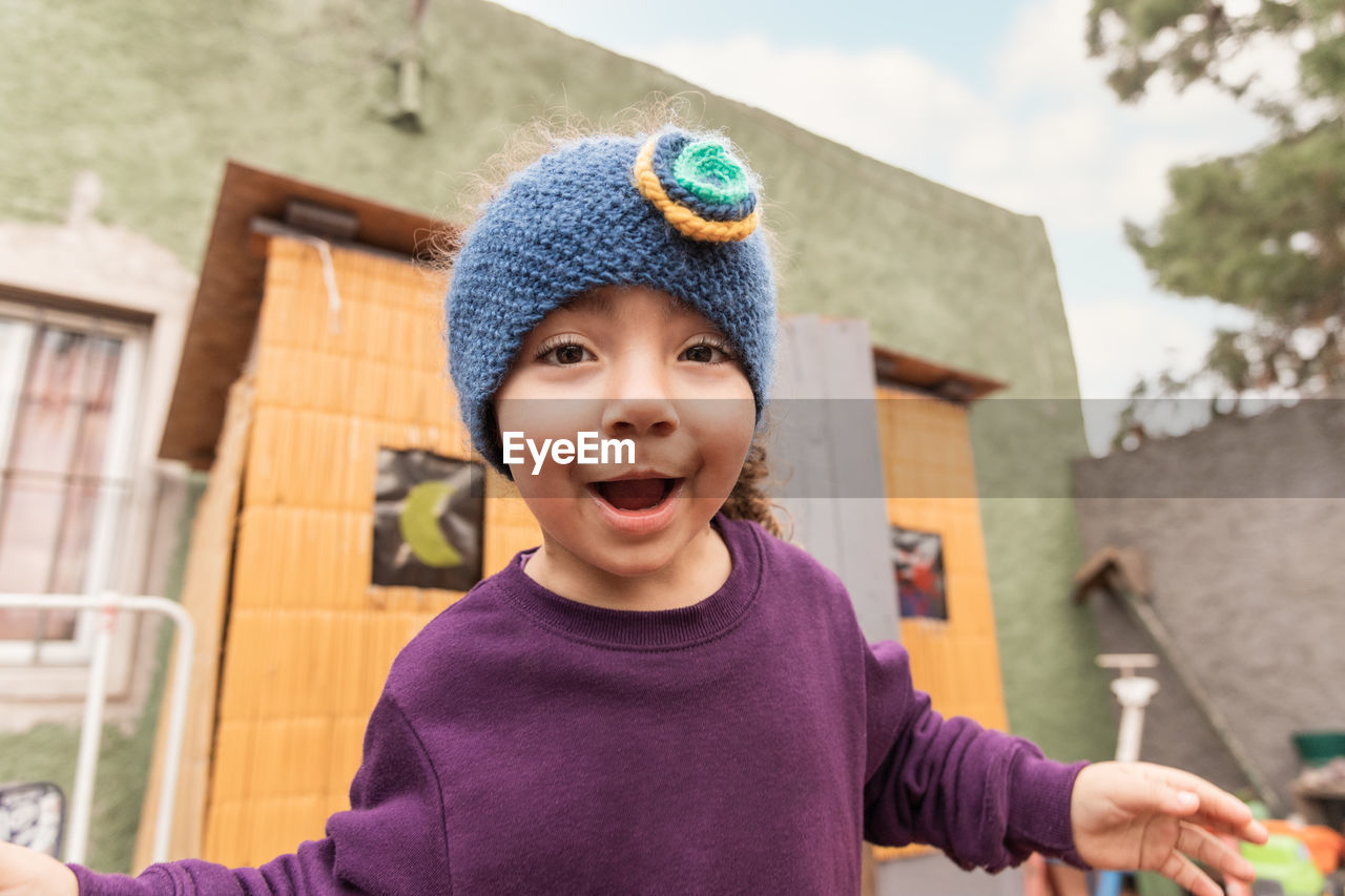 Delighted ethnic girl looking at camera with smile while standing on porch of cabin in countryside